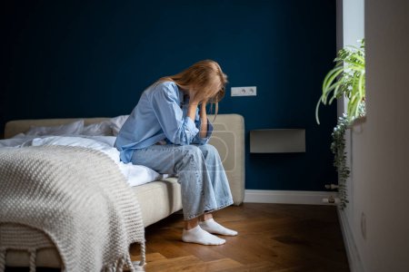 Photo for Unhappy loneliness woman lost in thoughts sitting on bed holding head in hand at home. Negative emotional pressure on female. Stressed girl thinking about problems, break up, divorce, feeling unwell - Royalty Free Image