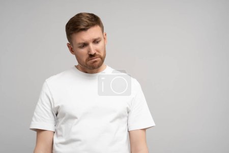 Sad disappointed man with head down on gray background. Portrait of young upset frustrated guy. Problems, depression, desperation, hopelessness, frustration concept. Negative human sincere emotions.
