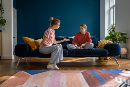 Photo for Upset teen girl sitting on sofa listening angry mother scolding her for bad school grades. Mom parent and teenage daughter having misunderstandings, sit on couch together at home and talking - Royalty Free Image