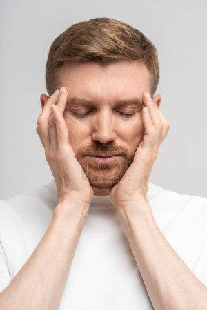 Photo for Irritated exhausted man with eyes closed presses fingers to temples from headache, failure, fatigue, difficult choose, isolated background. Overwhelmed male with professional burnout tries concentrate - Royalty Free Image