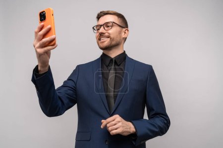 Photo for Successful man with smartphone. Middle aged businessman smiles looking at cellphone communicating via video chat with customers, trader talking to client director speaking to employees via online call - Royalty Free Image