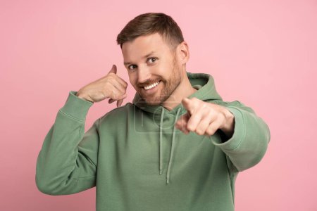Photo for Smiling laughing excited bearded man pointing index finger showing phone gesture call me on pink background looking at camera. Banner for advertisement, marketing. Unverbal communication concept. - Royalty Free Image