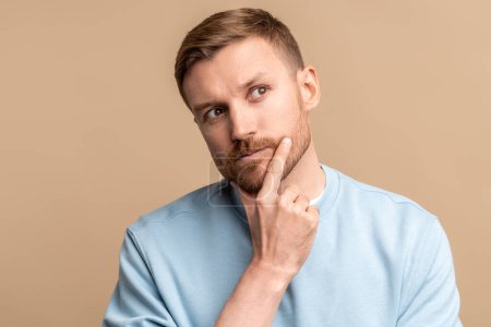 Photo for Thoughtful puzzled wistful man looking up touching chin by hand on beige background. Pensive guy trying make decision feeling frustration, uncertainty. Life problems, troubles, body language concept. - Royalty Free Image