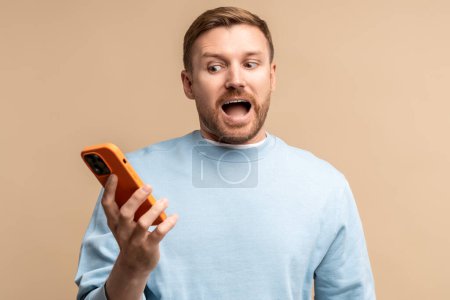 Photo for Shocked screaming confused man looking at smartphone screen on beige background. Sad desperated guy has bad news, loses money, life problems troubles. Emotional frustrated male feels disappointment. - Royalty Free Image