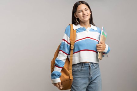 Photo for Happy smiling student teen girl with backpack, copy books on gray background. Portrait brunette cute friendly teenager in sweatshirt, jeans. Advertisement banner with copy space, education concept. - Royalty Free Image