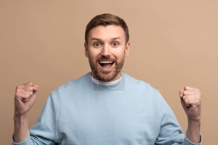 Photo for Happy cheerful man with crazy face expression showing win victory gesture on beige background looking at camera. Guy winner celebrates success, achieving goal. Body language, sincere emotions concept. - Royalty Free Image