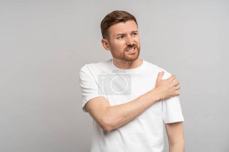 Photo for Man touching hand shoulder feeling pain isolated on gray background after injury, trauma. Neuralgia, pinched nerve in arm, broken fracture bruised arm. Health problems, bad symptom, painful concept. - Royalty Free Image