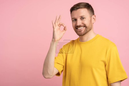 Photo for Positive happy man showing OK sign hand gesture on pink background with copy space looking at camera. Portrait smiling guy on advertisement banner, poster. Symbol of consent, confirmation concept. - Royalty Free Image