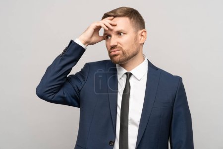 Tired confused frustrated businessman wears in official suit with dissatisfied face isolated studio background. Man touching forehead in tense thoughtful emotional state. Burnout, problem concept.