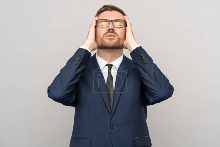 Photo for Confident exhausted tired depressed businessman, man entrepreneur in glasses, blue suit touching head with closed eyes on grey background. Burnout syndrome, life business troubles problems concept. - Royalty Free Image