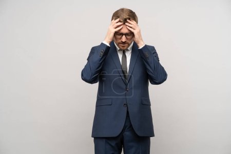 Photo for Tortured businessman trying to make decision, thinking hard about problems troubles on gray background. Man entrepreneur in suit glasses rubbing head with exhausted tired face. Headache, migraine. - Royalty Free Image
