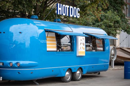 Téléchargez les photos : Camion de hot-dog bleu dans la rue vide en ville, camion de nourriture mobile. Café en transport avec menu à l'extérieur, cafétéria d'affaires. Infrastructure urbaine moderne dans le concept de restauration rapide malsaine de style vintage. - en image libre de droit