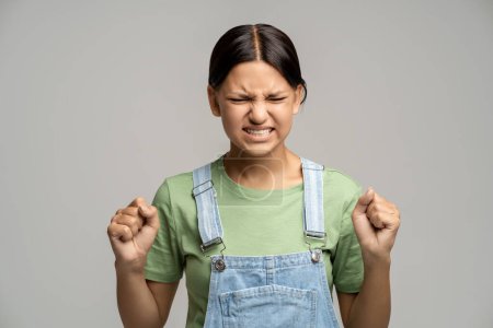 Photo for Angry frustrated teen girl clenched fists has evil frown face with closed eyes on grey background. Madly furious teenager viciously screaming shouting yelling. Sincere negative emotions concept. - Royalty Free Image