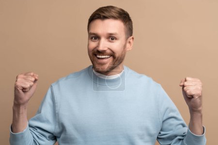 Photo for Happy cheerful man with crazy face expression showing win victory gesture on beige background looking at camera. Guy winner celebrates success, achieving goal. Body language, sincere emotions concept. - Royalty Free Image