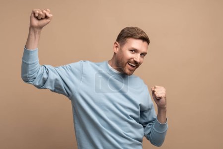 Photo for Happy man rejoices raising fists up. Middle aged guy smiles cheerfully happily brightly emotionally, expressively dances, celebrates victory win. Isolated on beige background, studio portrait for ad. - Royalty Free Image