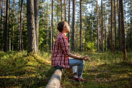 Photo for Relaxed man sitting on log in forest meditating on nature making spiritual practice. Guy relaxing resting feeling harmony, peace, tranquility, calm. Meditation, spiritual practice experience concept. - Royalty Free Image