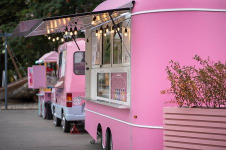 Photo for Pink ice cream vans on empty street in city, mobile fair trade with food trucks. Cafe in transport, cafeteria business. Modern urban infrastructure in vintage style, junk unhealthy food concept. - Royalty Free Image