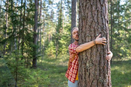 Foto de Hombre abrazando abrazando tronco de árbol en la naturaleza en el bosque con los ojos cerrados. Protección del medio ambiente, estilo de vida ecológico, actividades al aire libre en parques de ocio, dendrofilia, amante de las plantas, salvar el concepto de planeta. - Imagen libre de derechos