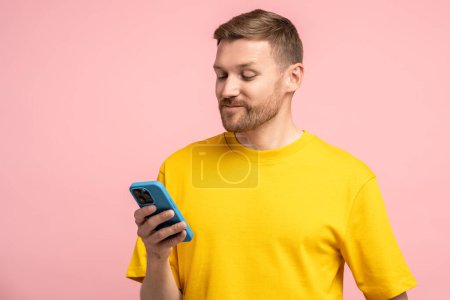 Photo for Pleased man holding smartphone, having video call, smiling while watching funny video, feeling happy winning online lottery bid. Middle-aged man looking at phone with relaxed expression on face - Royalty Free Image