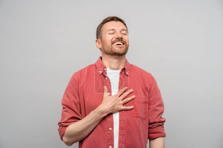 Photo for Happy positive cheerful man sincere laughing with closed eyes isolated on gray background. Bearded guy touching chest by hand enjoying feeling joy, gladness. Human emotions, hand gestures concept. - Royalty Free Image