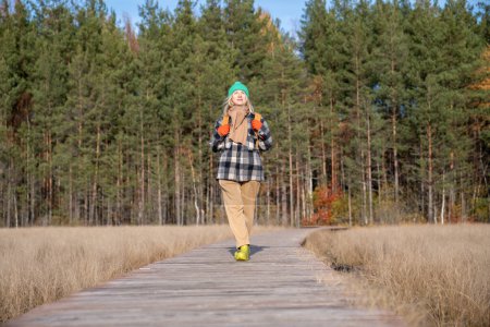 Photo for Middle aged tourist hiker woman walking along ecological trail in natural Scandinavian park with pine trees. Relaxed female enjoying pastime in unity with nature. Travel tourism wanderlust vacation. - Royalty Free Image