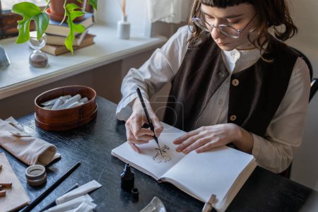 Photo for Creative artist-illustrator sketching with ink at cozy workplace. Serious girl in glasses creating white-black animation. Absorbing hobby, creative pastime, freelance work, professional occupation - Royalty Free Image