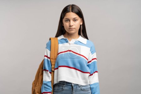 Photo for Focused teen student girl with backpack on shoulder isolated studio background. Serious unsmiling joyless young teenager schoolgirl looking at camera. Beginning of academic year, admission to college - Royalty Free Image