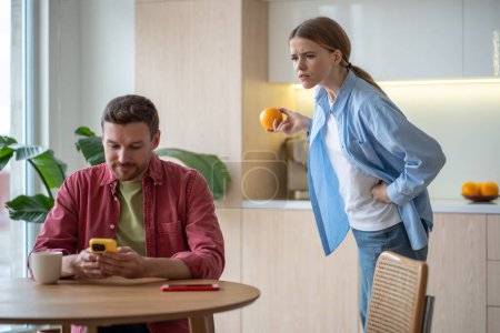 Photo for Jealous wife peeking looks at flirting man cellphone. Suspicious woman watches husband texting another woman. Dissatisfied girl in kitchen with unfaithful boyfriend. Checking, mistrust relationship. - Royalty Free Image