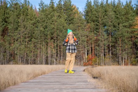 Photo for Calm middle-aged woman delighted with warm autumn sunny day standing on nature trail turning face toward sun. Pleased female relaxing in silence while hiking in scandinavian pine forest reserve - Royalty Free Image