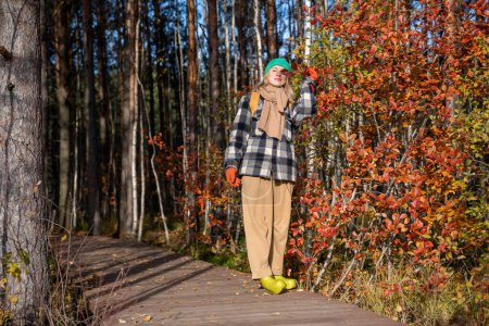 Téléchargez les photos : Femme d'âge moyen marchant seule dans un parc d'automne paysager, debout près d'un arbre à feuilles rouges, les yeux fermés, profitant de la nature. Touriste féminine voyageant en écotrope dans la forêt scandinave en vacances d'automne. - en image libre de droit
