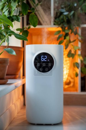 Photo for Ultrasonic humidifier with sensor near windowsill with potted houseplants flowers spraying water vapor steam. Humidification dry air at home apartment for comfort atmosphere of people plants concept. - Royalty Free Image