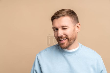 Photo for Flirting man winks look at camera, studio portrait isolated on beige. Bearded middle aged guy smiling winking playfully jokingly impishly with one eye, hinting, hidden intent, non-verbal communication - Royalty Free Image