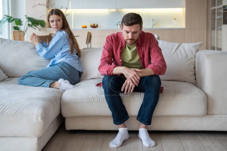 Photo for Gloomy upset passive man sitting on sofa apathetically looking on floor with blank stare, and offended woman with reproaching face expression. Misunderstanding, confrontation, crisis in family life - Royalty Free Image