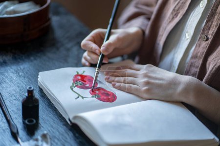 Photo for Girl art student painting sketches tomatoes in sketchbook sitting at desk in art school university college workshop class. Paint lesson, practice, improving skills concept. Hands with brush close-up. - Royalty Free Image