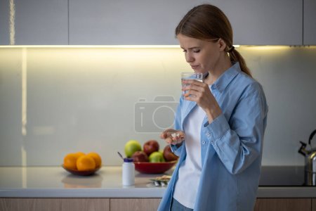 Photo for Unhealthy, suffering from pain, chronic ache woman holding pills, painkillers, antibiotics on palm, glass of water, going to take treatment. Depressed frustrated woman feeling uncomfortable, unwell - Royalty Free Image