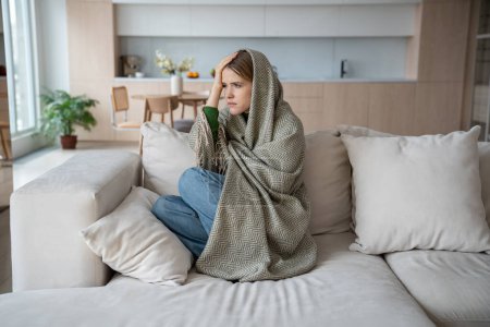 Photo for Emotional burnout of young woman sitting on couch wrapping in plaid with headache. Depressed female feeling apathy, anhedonia suffering from mental disorder, depression. Highly sensitive person. - Royalty Free Image