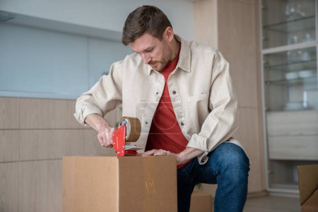 Photo for Serious tired man packing cardboard boxes on kitchen to move new apartment. Guy preparing to relocate in other flat, house. Relocation, mortgage, loan, life changings, buying real estate concept. - Royalty Free Image