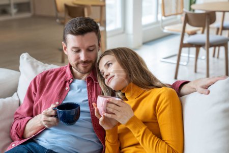 Photo for Devoted happy woman holding cup of tea leaning head on shoulder of beloved man. Cheerful man looks at female with loving glance. Love, romance, tenderness, togetherness, closeness in relations - Royalty Free Image