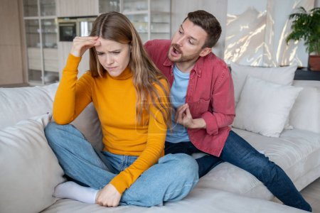 Photo for Abusive husband screaming at wife sitting on couch at home, tears streaming down face as turns away in emotional distress. Jealous man tyrant have scandal threatens sad woman. Family quarrel betrayal. - Royalty Free Image