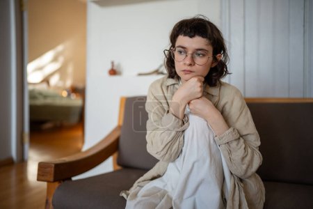 Photo for Thoughtful bored lonely teen girl in glasses feeling apathy sitting on couch at home. Teenager suffer from depression, mental disorder, anhedonia, stress. Burnout syndrome after stress life period. - Royalty Free Image