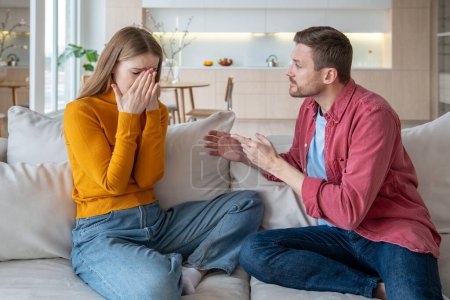 Photo for Jealous furious man talk scream at crying woman wife sitting on couch at home. Family quarrel, scandal of two spouses. Tyrant husband threatens woman. Betrayal infidelity mistrust, couple relations. - Royalty Free Image