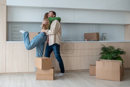 Photo for Overjoyed wife and husband hugging on kitchen moving to new flat among cardboard boxes. Relocation, family mortgage, buying apartment, real estate. Happy emotional couple spouses enjoying life changes - Royalty Free Image