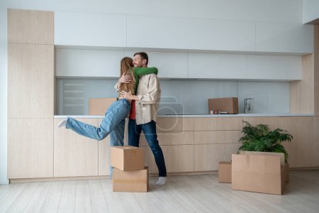 Photo for Glad joyful wife hugging of happiness cheerful smiling husband. Married couple standing among packed cardboard boxes, moving into new flat, apartment, house. Independent living, buying own property - Royalty Free Image
