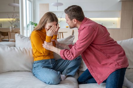 Photo for Aggressive stressed tyrant man husband shouts grabs wife by arms. Unhappy scared woman crying closing face by hands sitting at home. Domestic physical, emotional violence, family quarrel, gaslighting. - Royalty Free Image