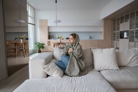 Photo for Sad tired woman sits on couch at home wrapped in plaid in living room. Blue mood of depressed girl boring. Nervous female feeling frustration hiding from society in loneliness solitude. Life problems. - Royalty Free Image