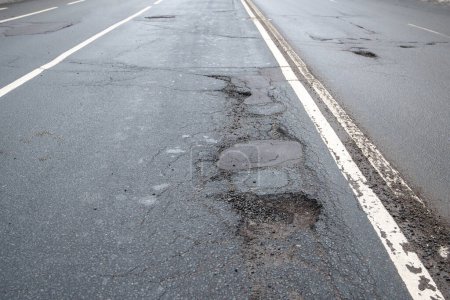 Photo for Broken asphalt road in city and untimely repair. Pothole asphalt with road markings. Roadway in bad condition need of repair. Prolonged repair of urban infrastructure. - Royalty Free Image