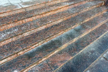Deicing chemicals on stairs in winter. Salt grains on icy stone steps in cold season. Slippery surface sprinkled with technical salt and calcium, above view. Prevent slipping concept