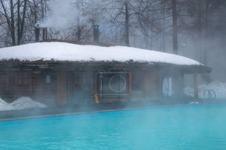 Photo for Wellness spa resort with hot outdoor empty swimming pool with thermal water in winter day surrounded with trees near bath and sauna. Foggy weather. - Royalty Free Image