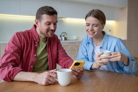 Photo for Cheerful happy woman and glad smiling man spend free time, weekend enjoying tea, coffee drinking, surfing in internet, scrolling social networks. Independent living, joint residence, marriage concept - Royalty Free Image