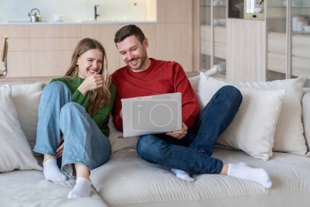 Glad joyful married couple laughing happily, looking into laptop computer screen. Cheerful wife and husband staying at home during lockdown, spending time together, watching comedies, funny videos